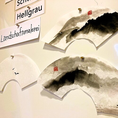 Whiteboard daran angepinnt Sumi Zeichnungen und Übungsaufträge
