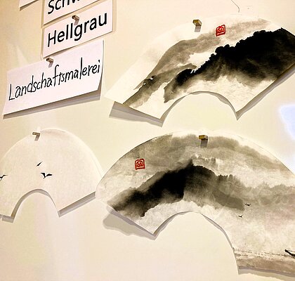 Whiteboard daran angepinnt Sumi Zeichnungen und Übungsaufträge