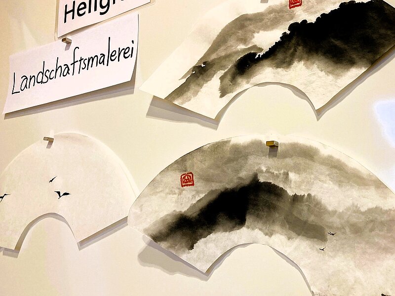 Whiteboard daran angepinnt Sumi Zeichnungen und Übungsaufträge