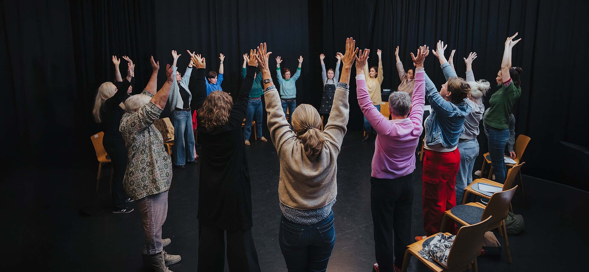 Teilnehmende im Kreis auf der Kreativ-Hausbühne, alle heben die Hände