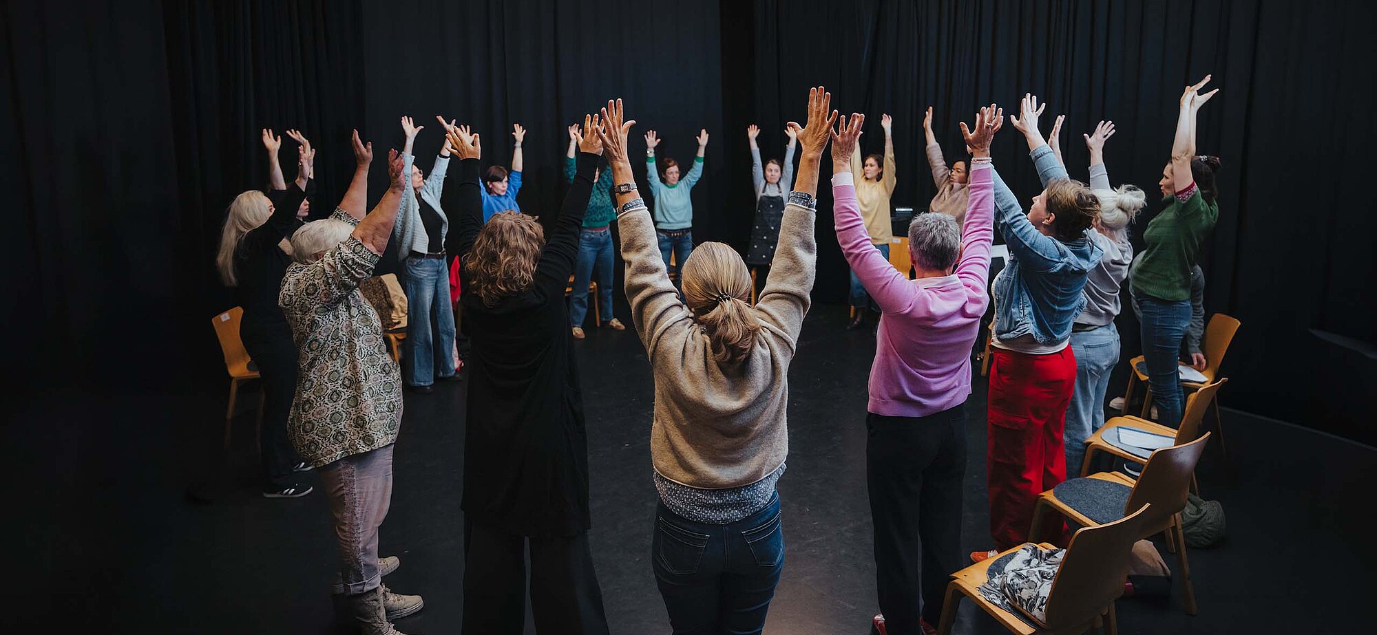 Teilnehmende im Kreis auf der Kreativ-Hausbühne, alle heben die Hände