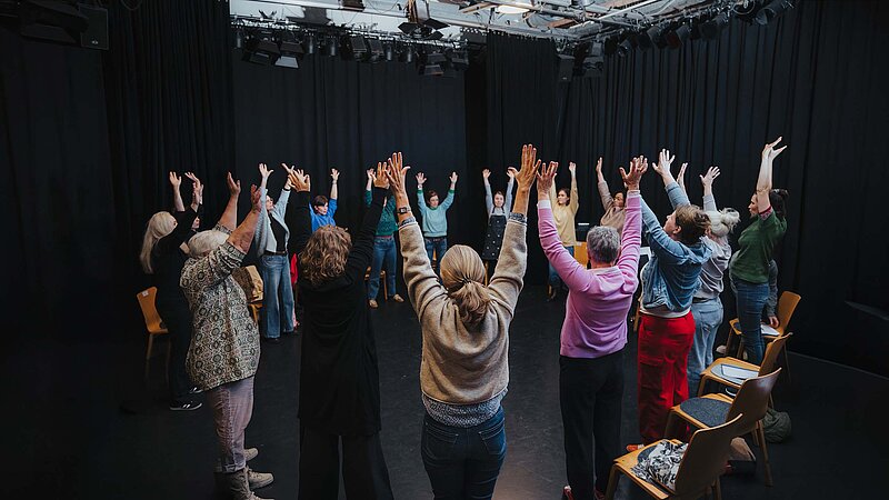 Teilnehmende im Kreis auf der Kreativ-Hausbühne, alle heben die Hände