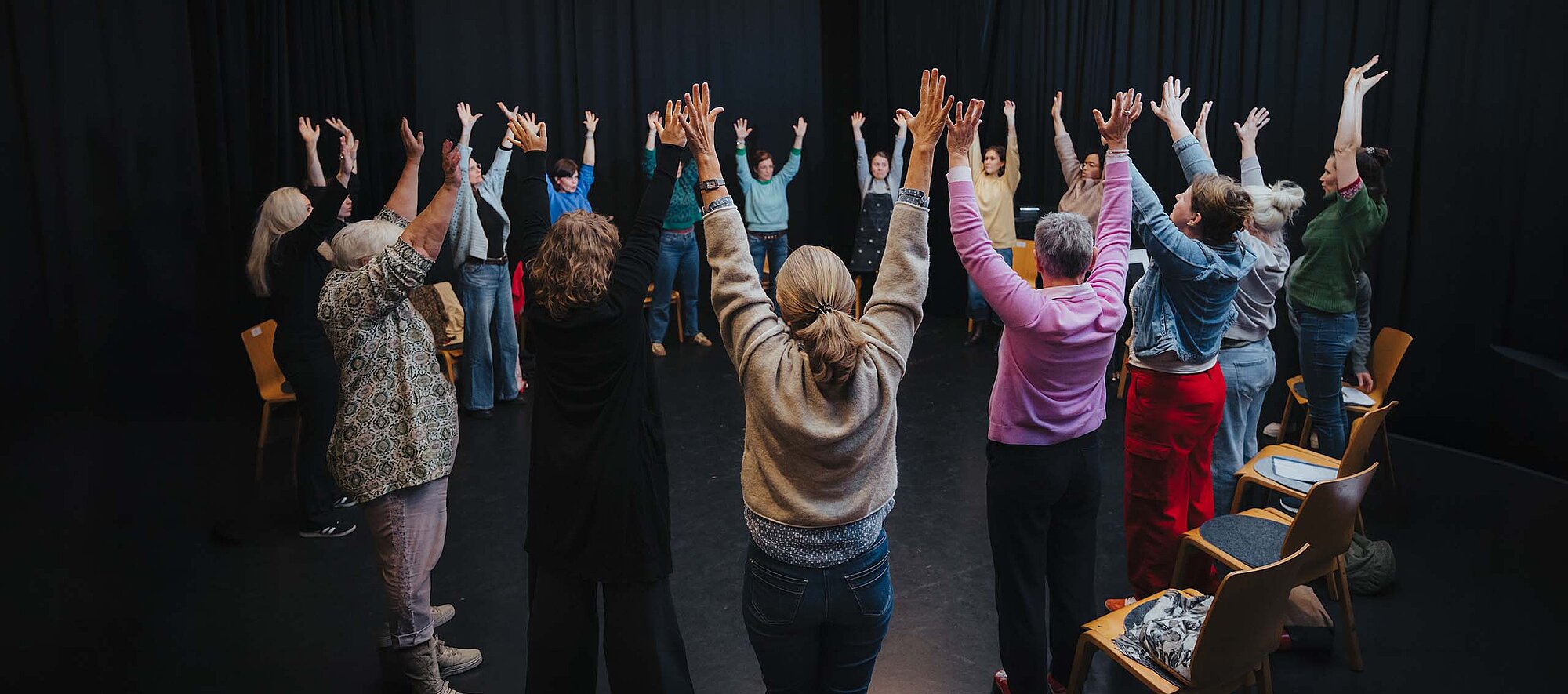 Teilnehmende im Kreis auf der Kreativ-Hausbühne, alle heben die Hände