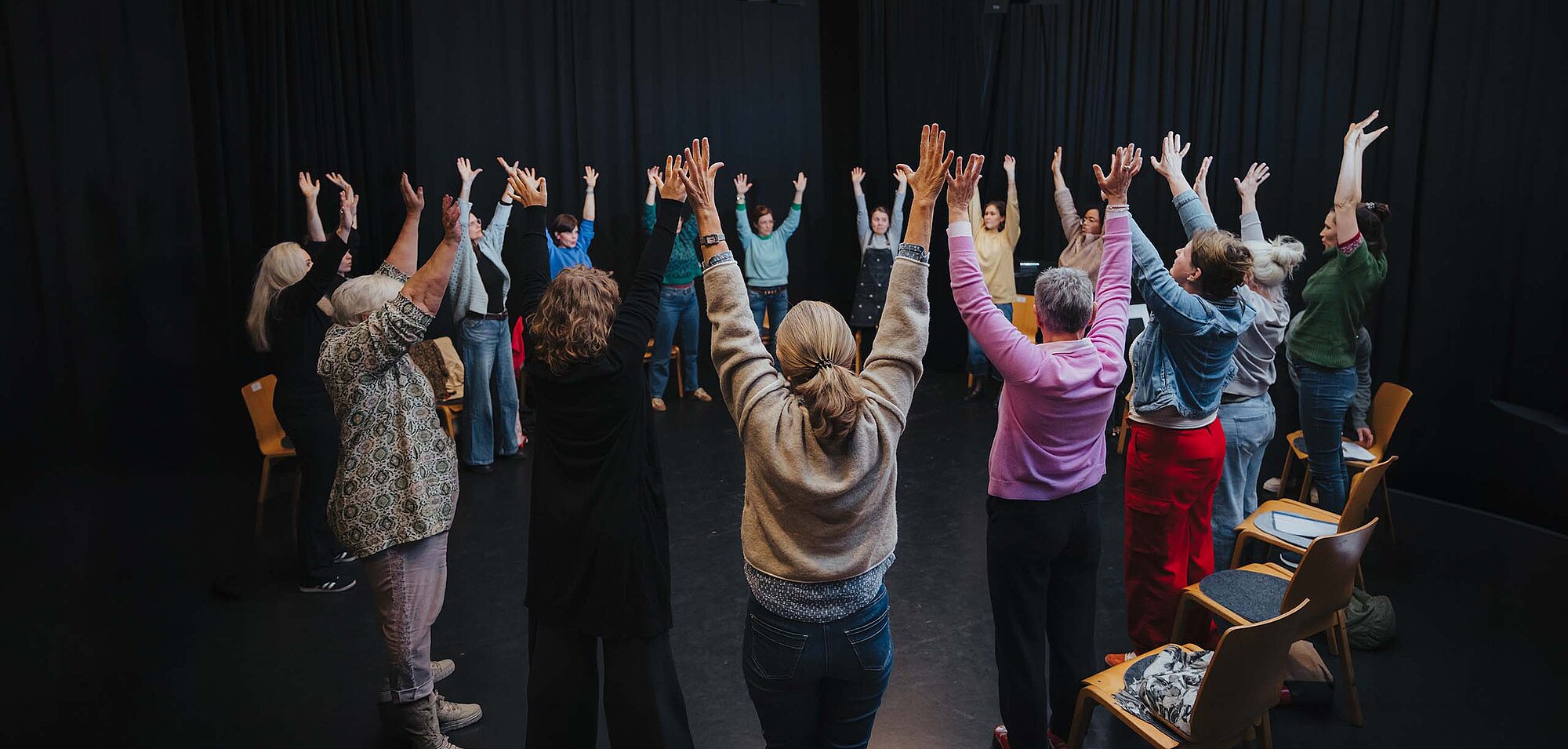 Teilnehmende im Kreis auf der Kreativ-Hausbühne, alle heben die Hände