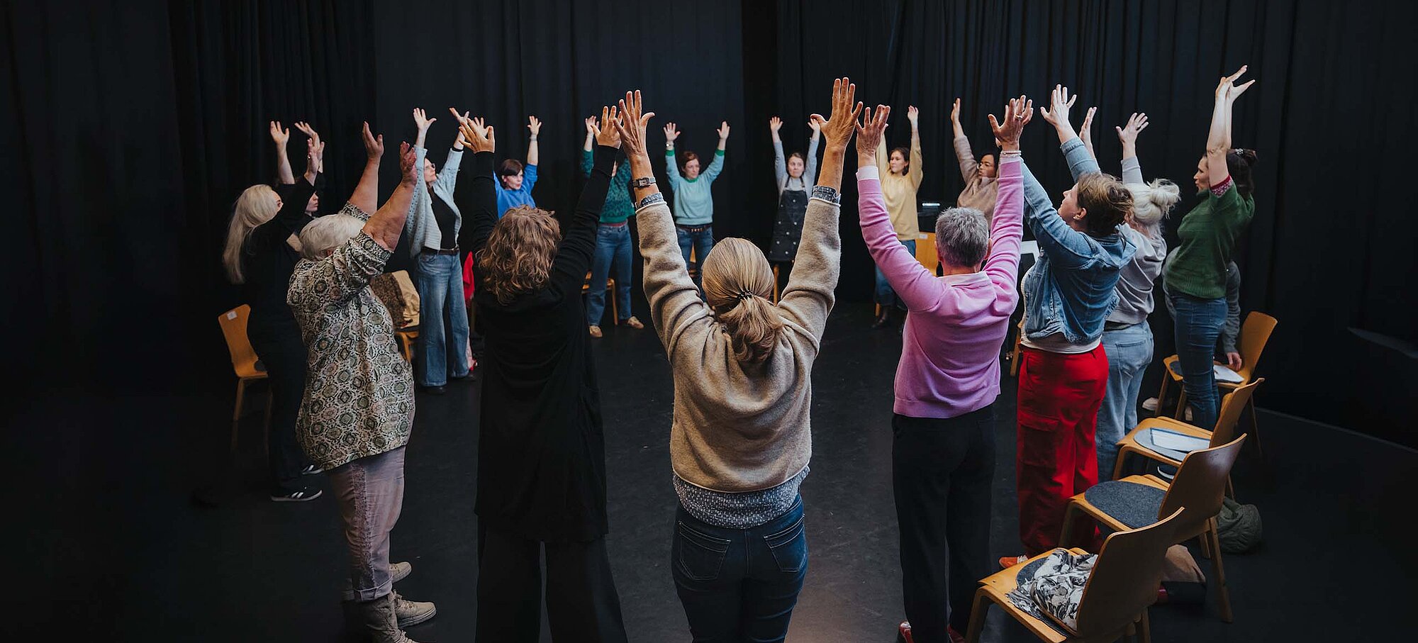 Teilnehmende im Kreis auf der Kreativ-Hausbühne, alle heben die Hände