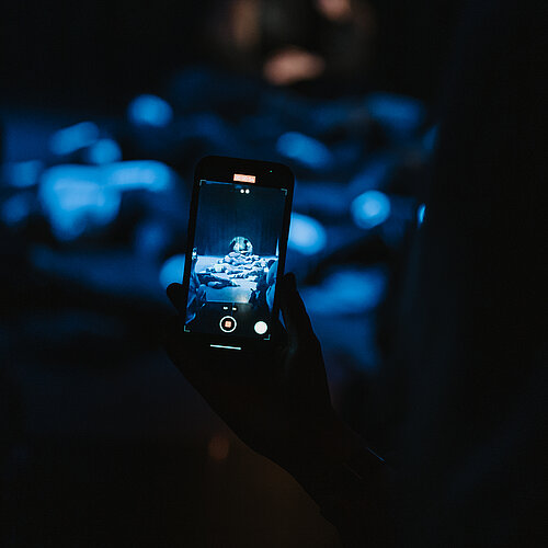 Hand hält Handy und filmt Bühnenauftritt in der Jugendkunstschule im Kreativ-Haus