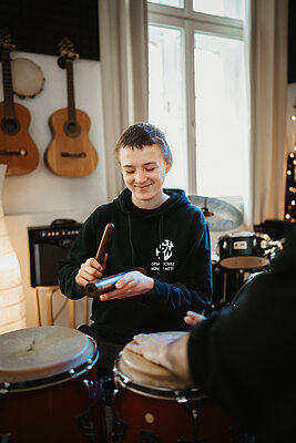 Ein Junge spielt Klanghölzer während Hände von jemandem auf Trommeln schlagen