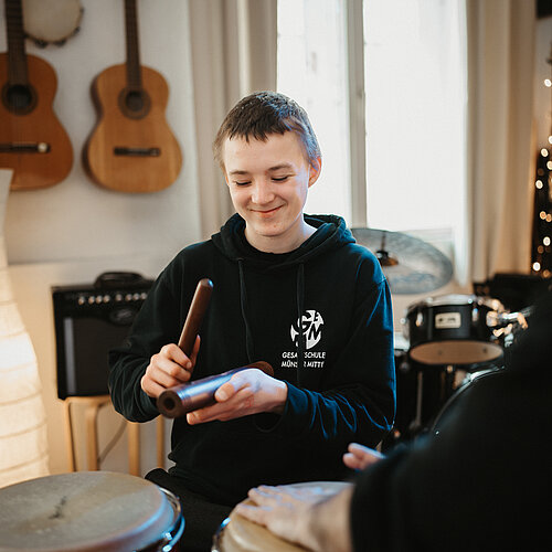 Ein Junge spielt Klanghölzer während Hände von jemandem auf Trommeln schlagen
