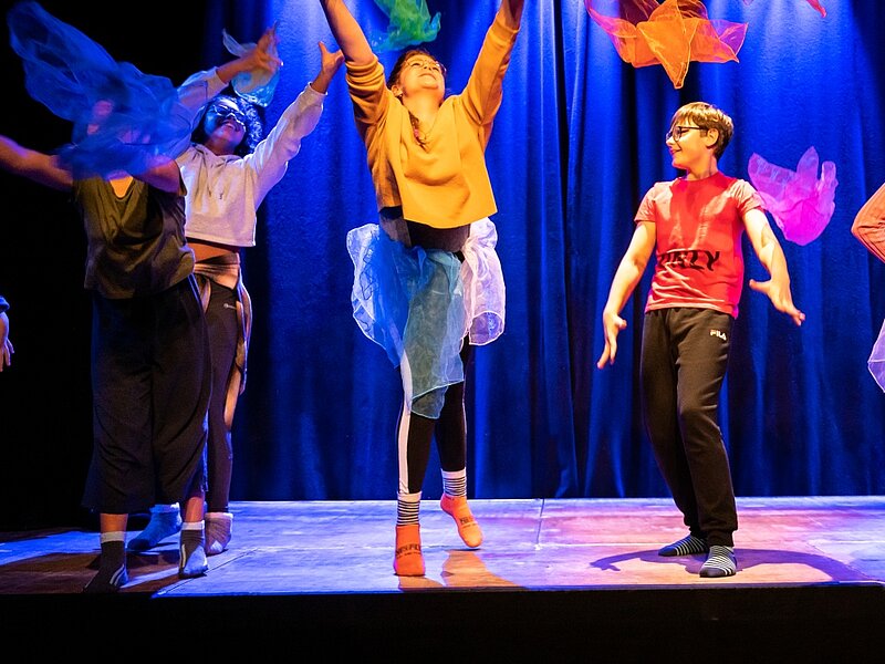 Kinder mit bunten Tuechern auf der Buehne bunt gekleidet bunt beleuchtet 