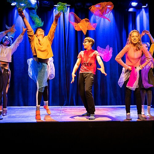 Kinder mit bunten Tuechern auf der Buehne bunt gekleidet bunt beleuchtet 