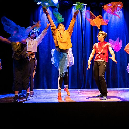 Kinder mit bunten Tuechern auf der Buehne bunt gekleidet bunt beleuchtet 