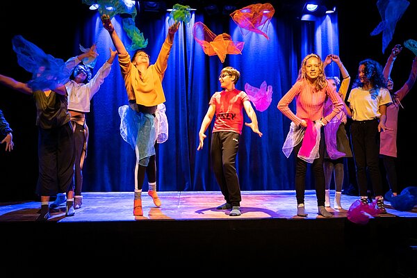 Kinder mit bunten Tuechern auf der Buehne bunt gekleidet bunt beleuchtet 