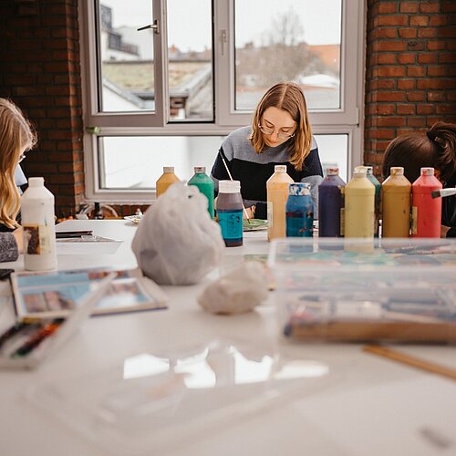 drei jugendliche Maedchen am Werktisch malen mit Acrylfarbe