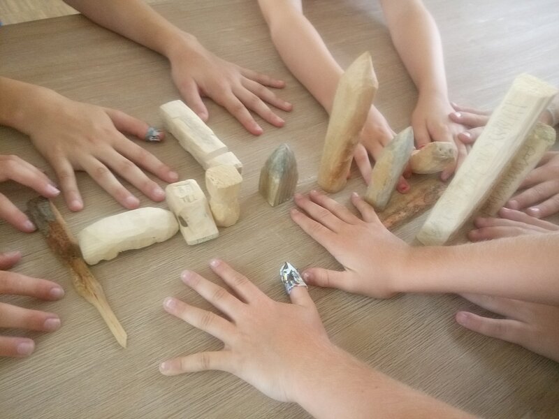 12 KinderHaende flach auf dem Tisch liegend in der Mitte ihre geschnitzten Holzformen