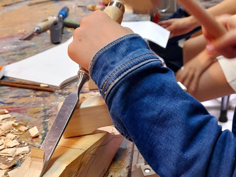 Hände mit Hammer und Meißel bearbeiten Holzblock in der Schnitzwerkstatt der Jugendkunstschule im Kreativ-Haus