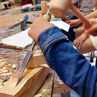 Hände mit Hammer und Meißel bearbeiten Holzblock in der Schnitzwerkstatt der Jugendkunstschule im Kreativ-Haus