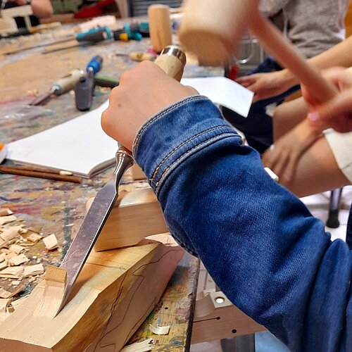 Hände mit Hammer und Meißel bearbeiten Holzblock in der Schnitzwerkstatt der Jugendkunstschule im Kreativ-Haus