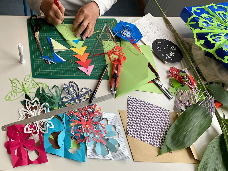 Verschiedene Scherenschnitte in buntem Papier und Haende im Schnittvorgang