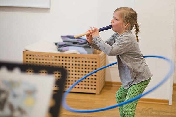 Maedchen spielt Blockfloete und kreist dabei mit der Huefte einen Gymnastikreifen