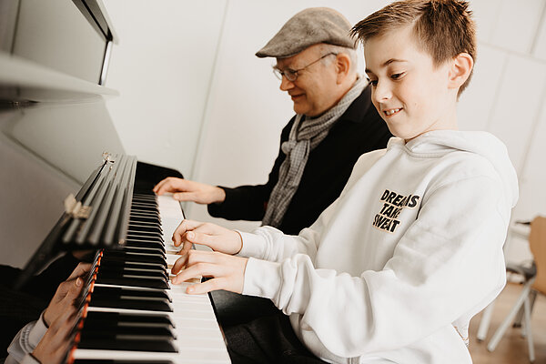 Ein Junge und ein Mann sitzen nebeneinander an einem Klavier und spielen die Tasten