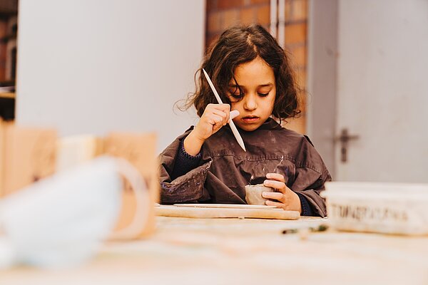 Maedchen an Werktisch bearbeitet konzentriert ein getaopertes Gefaess mit einem Werkzeug