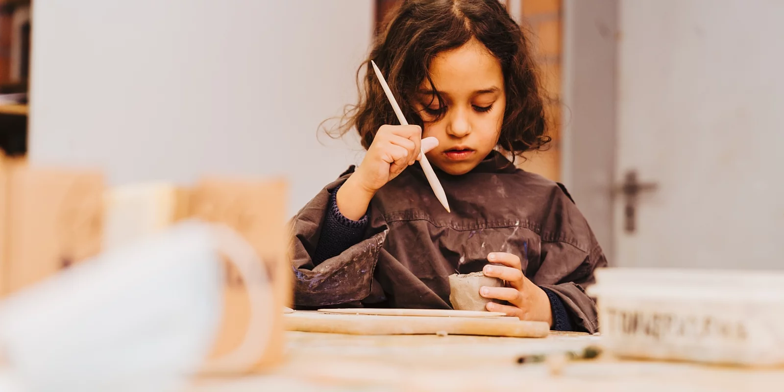 Maedchen an Werktisch bearbeitet konzentriert ein getaopertes Gefaess mit einem Werkzeug