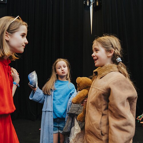 2 Kinder im Vordergrund und zwei Kinder im Hintergrund spielen eine Theaterszene auf der Buehne