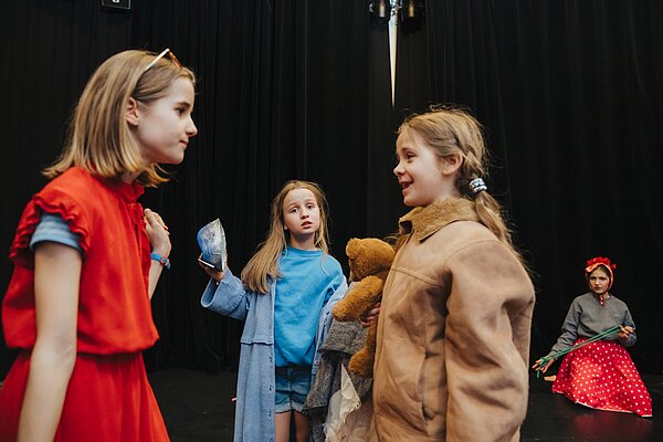 2 Kinder im Vordergrund und zwei Kinder im Hintergrund spielen eine Theaterszene auf der Buehne