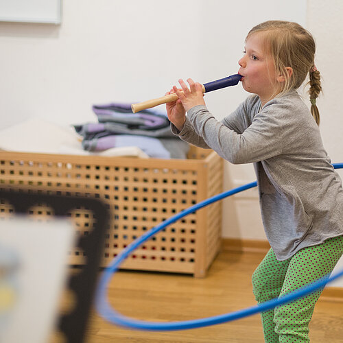Mädchen spielt Blöckflöte und dreht einen Hulahoop Reifen um ihre Hüfte