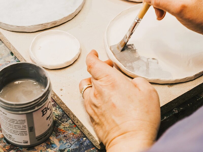 Einblick Töpferkurs, Hände glasieren getöpferten Teller