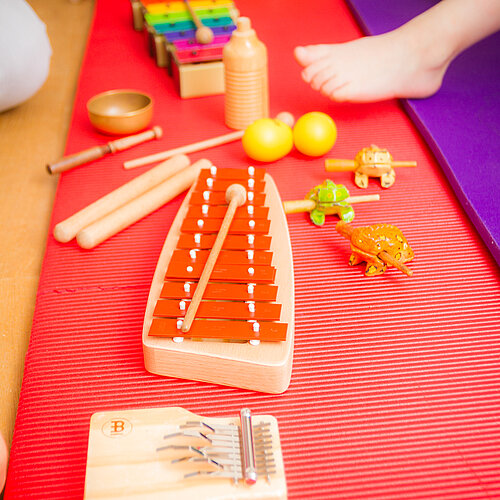 verschiedene Musikinstrumente sind aufgereiht: ein Tamburin, ein Xylofon, Rasseln, eine Klangschale, Klangfrösche