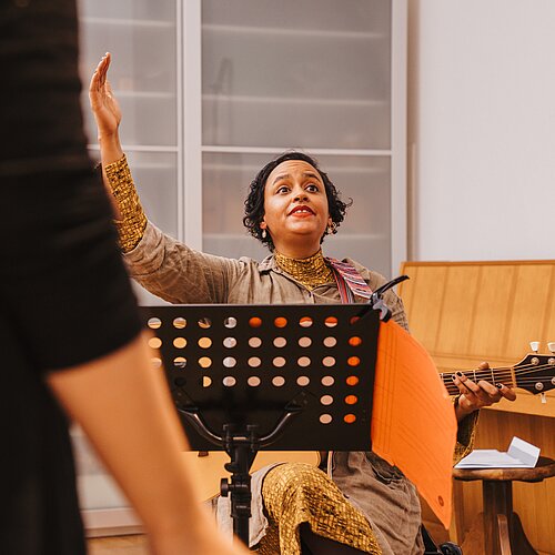 Sitzende Chorleiterin mit Gitarre hinter Notenstaender