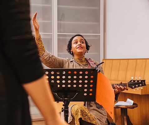 Sitzende Chorleiterin mit Gitarre hinter Notenstaender