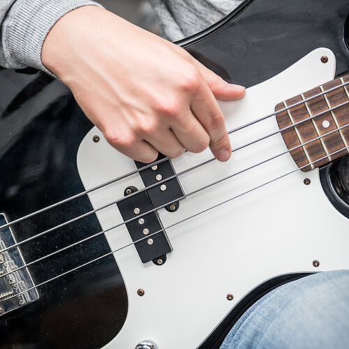 Eine Hand spielt die Saiten einer Bass Gitarre