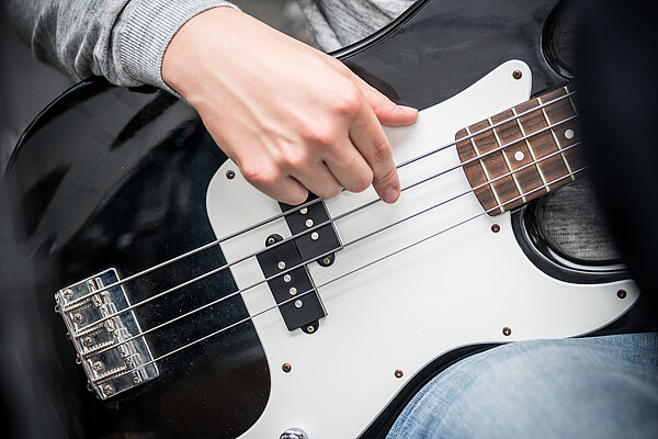 Eine Hand spielt die Saiten einer Bass Gitarre