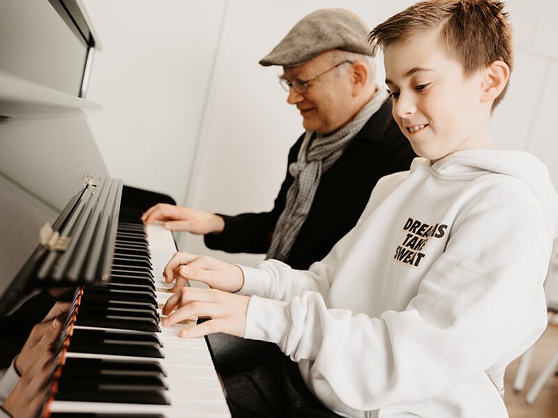 Ein Junge und sein Klavierlehrer spielen nebeneinander sitzend auf einem Piano