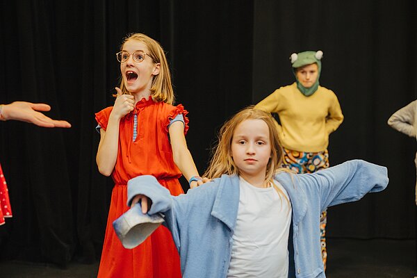 Drei Kinder spielen auf der Buehne eine Theaterszene im Kostuem