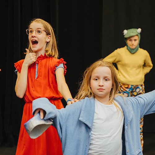 Drei Kinder spielen auf der Buehne eine Theaterszene im Kostuem