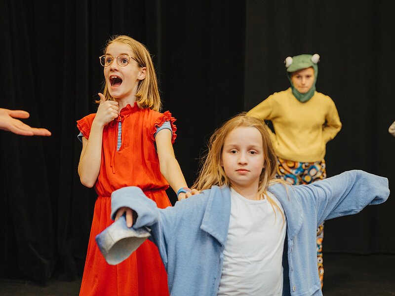 Drei Kinder spielen auf der Buehne eine Theaterszene im Kostuem